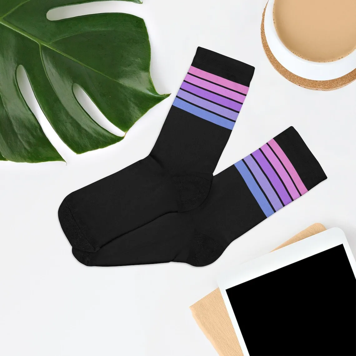 Bisexual pride striped socks arranged beside a plant and coffee